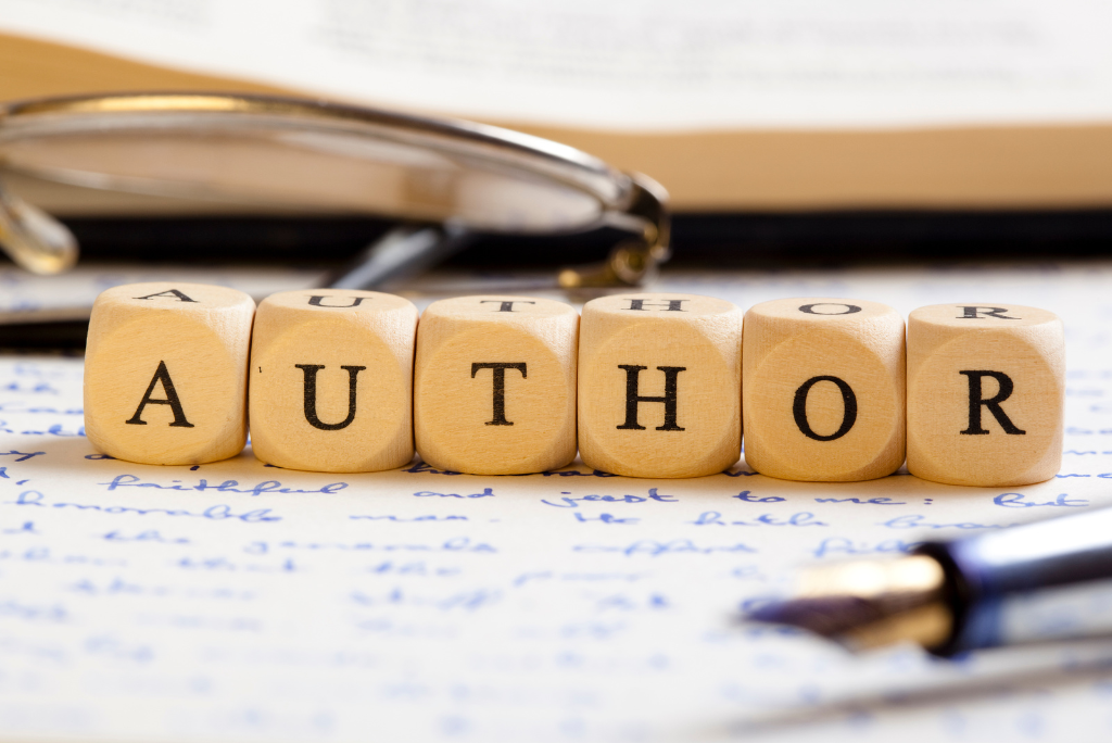 Wooden blocks spelling "AUTHOR" with a fountain pen and eyeglasses on a handwritten paper, symbolizing writing and creativity.