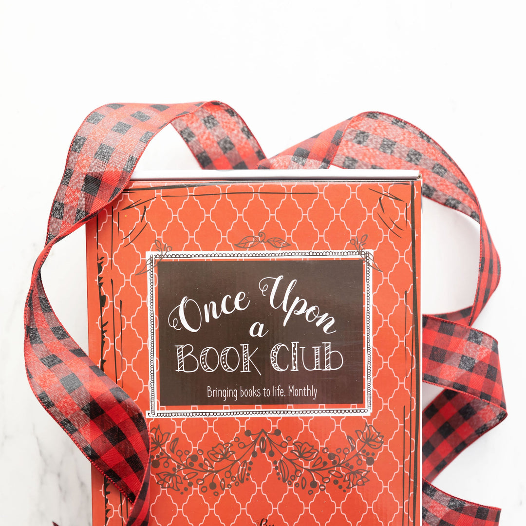 A vibrant red box with a black and red plaid ribbon labeled "Once Upon a Book Club" featuring a festive holiday-themed design.