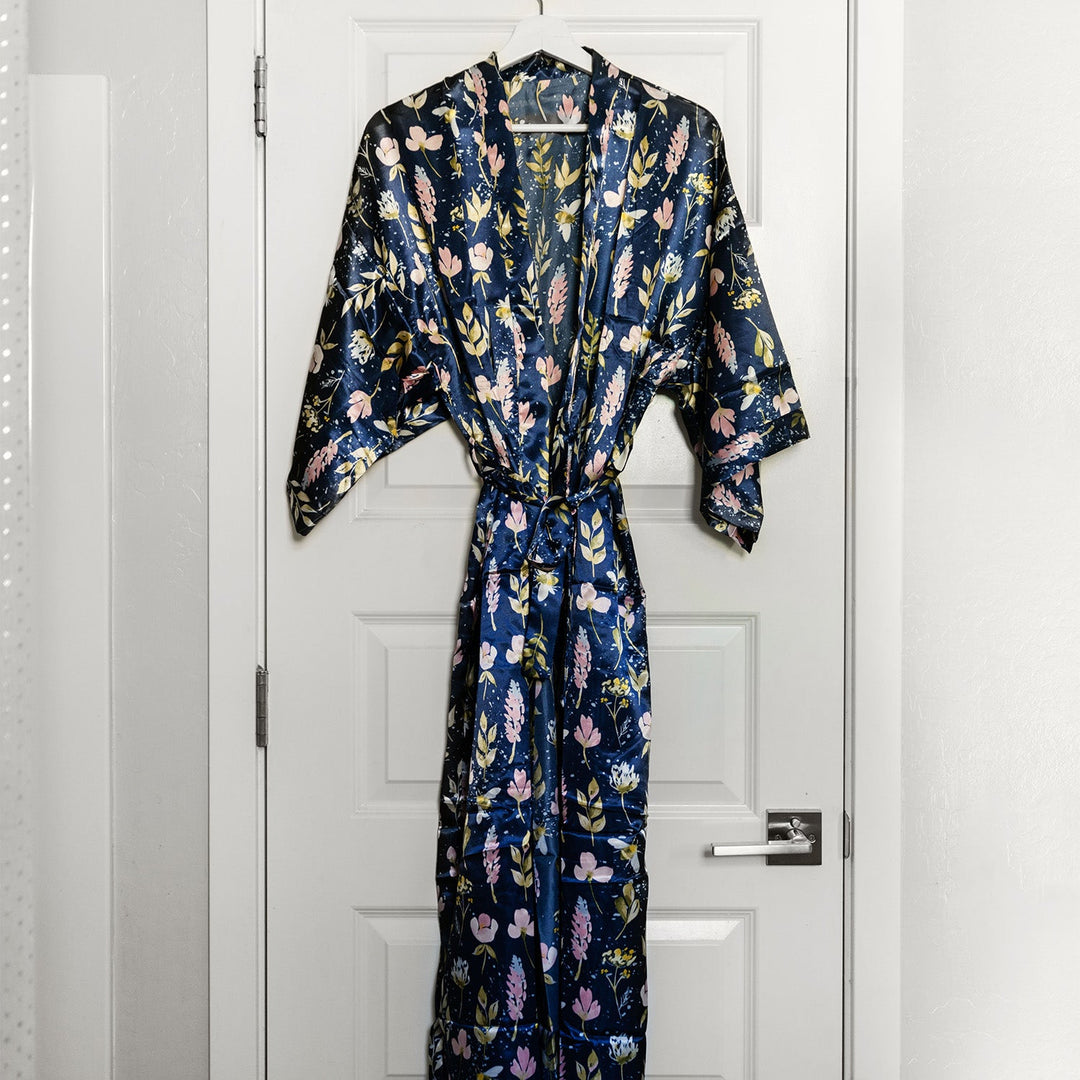 Floral satin robe in navy blue with pastel accents hanging neatly on a white door, showcasing an elegant and stylish design.