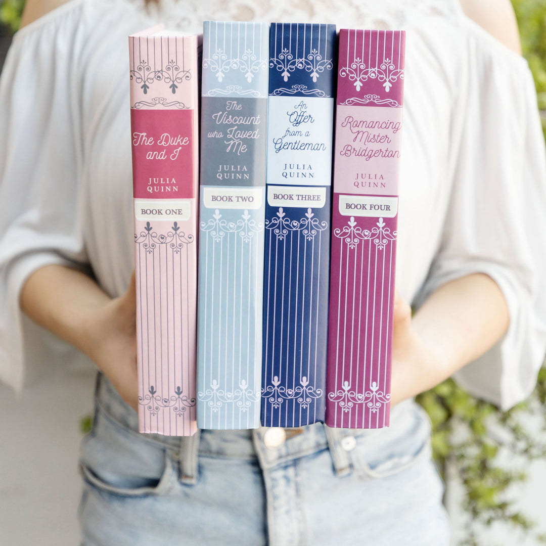 A person holding the first four books of the Bridgerton series by Julia Quinn, featuring pastel and jewel-toned spines with elegant designs.