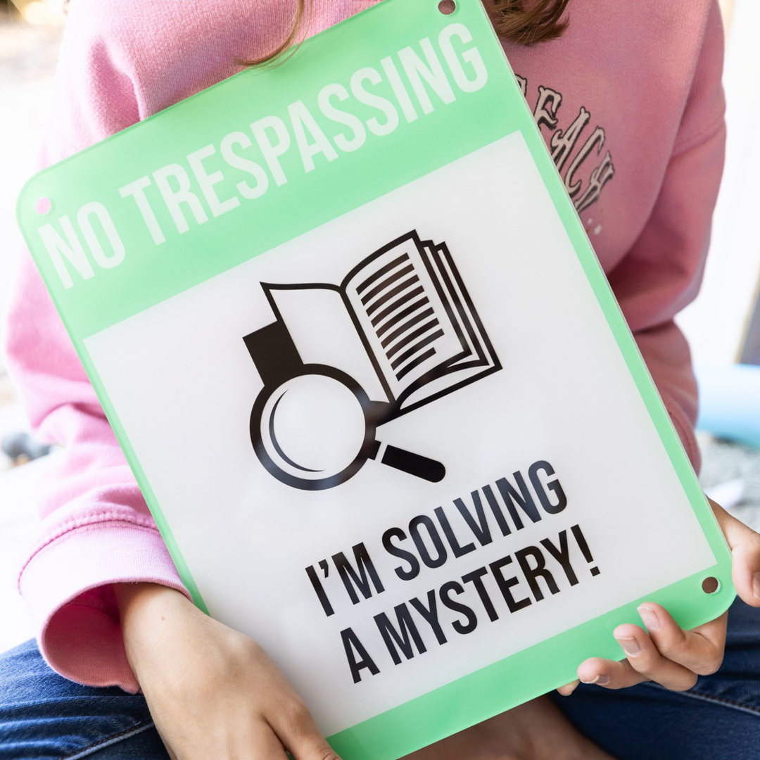A pair of white hands holds a large door sign that reads "No Trespassing, I'm Solving a Mystery" and features a magnifying glass and an open book in the middle of the image.