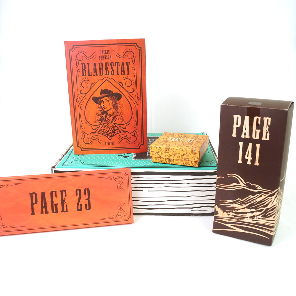 A green box lays on a white background. On top of the box is a hardcover, exclusive edition of BLADESTAY by Jackie Johnson featuring an orange cover with black detailing including a girl in a cowboy hat. Surrounding this are three gift boxes wrapped in various, western-themed packaging labeled with page numbers meant to only be opened when you reach the designated page number.