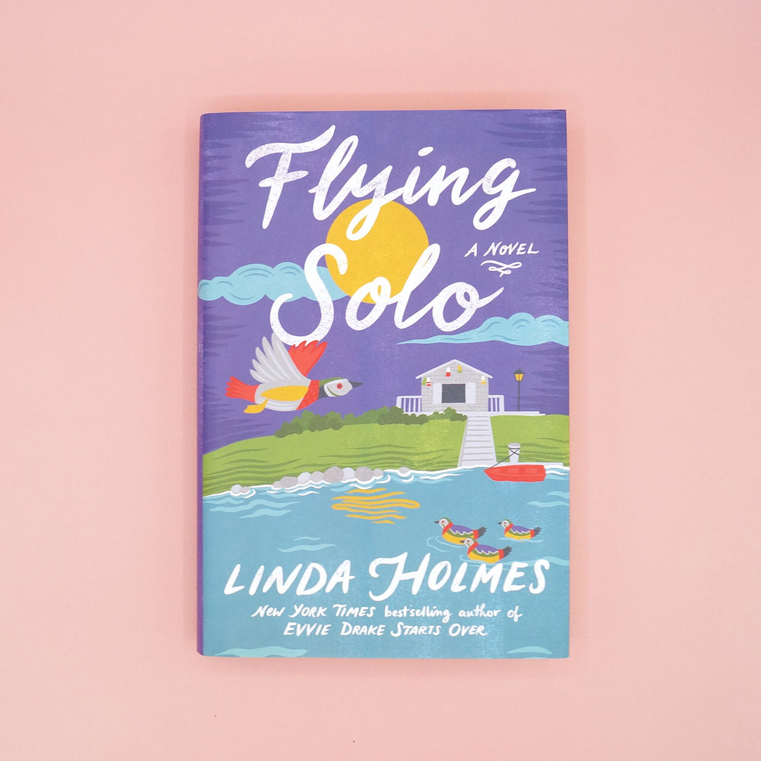 A hardcover copy of Flying Solo by Linda Holmes on a pink background.