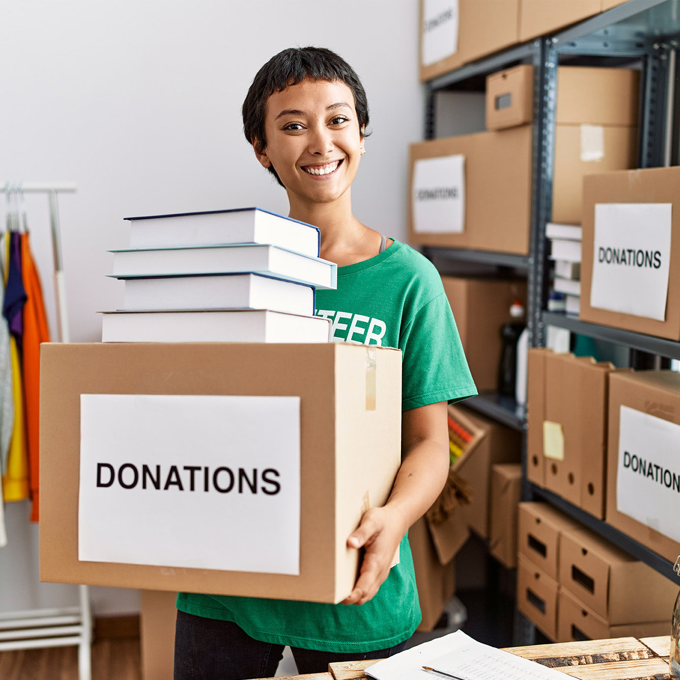 A smiling woman wearing a green volunteer t-shirt holds a box labeled