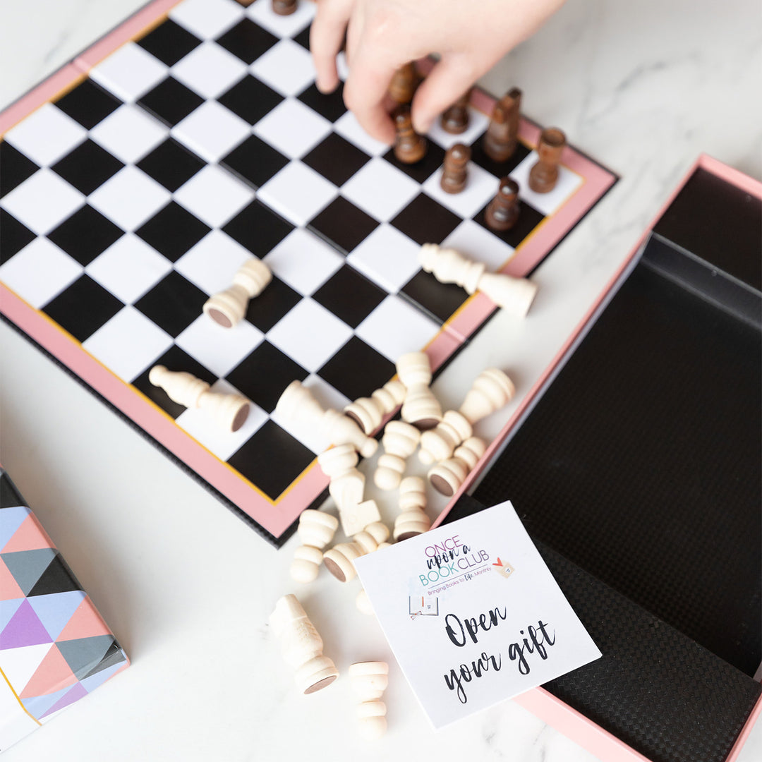 A close up on the pink-bordered chess set featuring dark wood and light wood pieces. An open your gift sticky note is at the bottom of the image.
