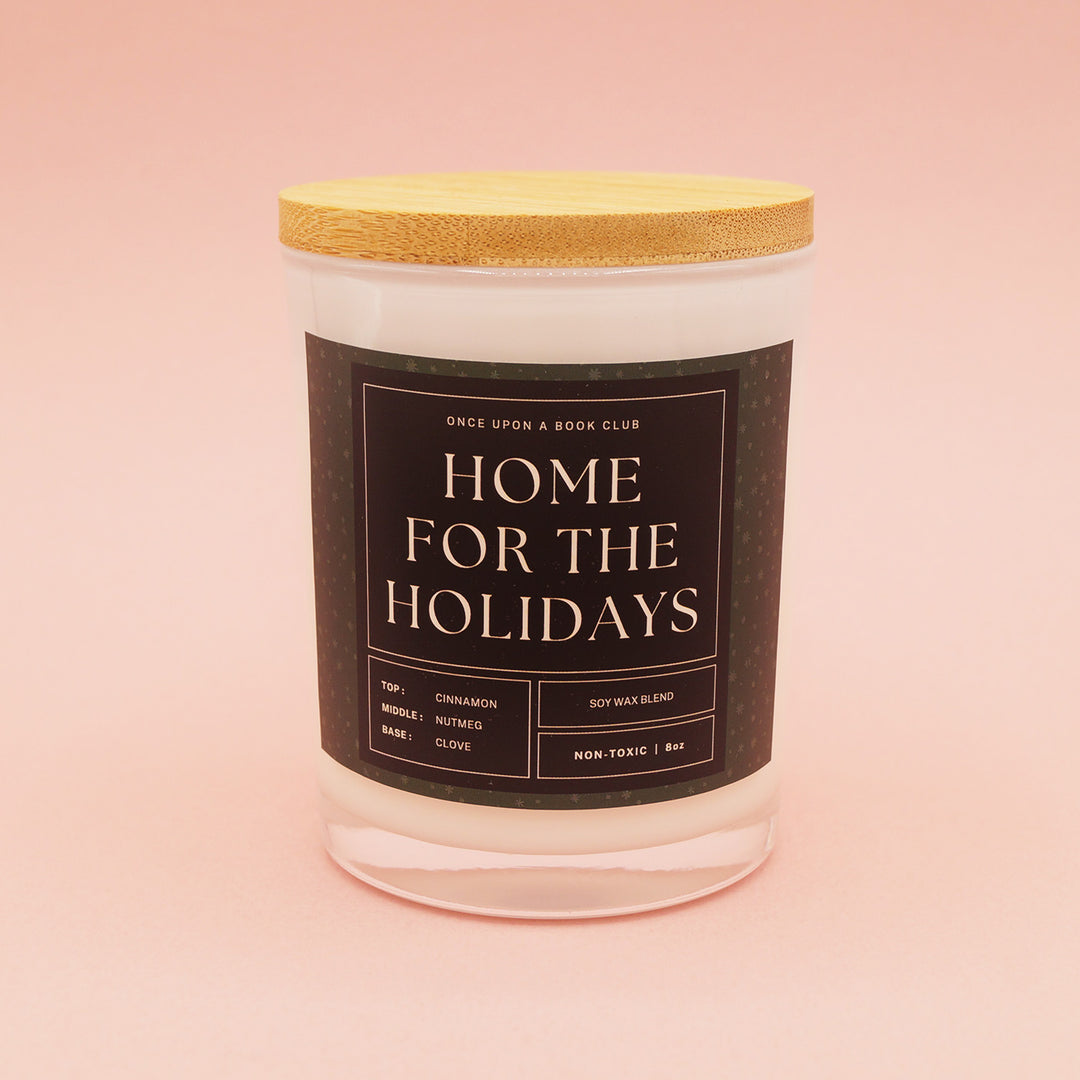 An 8oz glass candle jar that reads "Once Upon a Book Club, Home for the Holidays". On a pink background