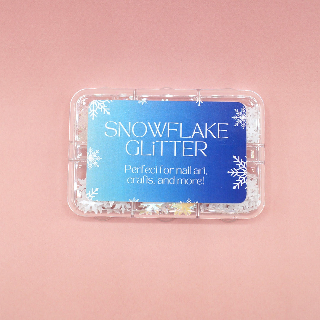 Snowflake Glitter tray containing six different sizes/shapes of snowflake glitter. Perfect for nail art, crafts, and more! On a pink background