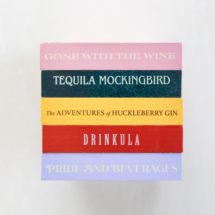 A set of five drink coasters featuring drink puns from classic novels including "Drinkula", "Tequila Mockingbird", "Gone with the Wine", "The Adventures of Huckleberry Gin", and "Pride and Beverages".