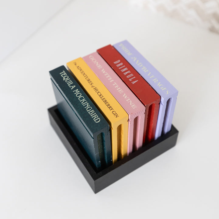 A set of five drink coasters featuring drink puns from classic novels including "Drinkula", "Tequila Mockingbird", "Gone with the Wine", "The Adventures of Huckleberry Gin", and "Pride and Beverages".