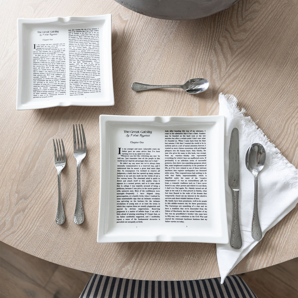 Two dinner plates with The Great Gatsby text, paired with silver cutlery on a wooden dining table.