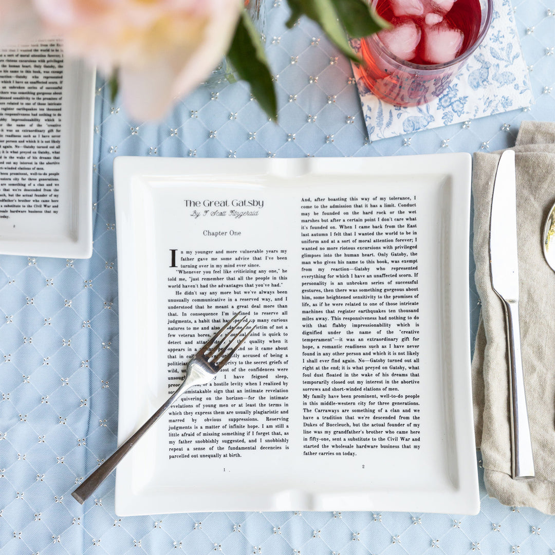 Dinner plate with The Great Gatsby text, set with cutlery on a patterned blue tablecloth.