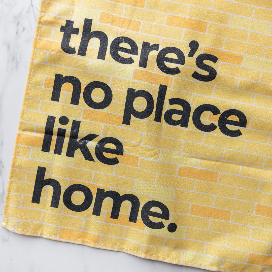 A close up of the yellow brick pattern on the tea towel. The words "There's no place like home" are printed in bold black letters over the pattern.