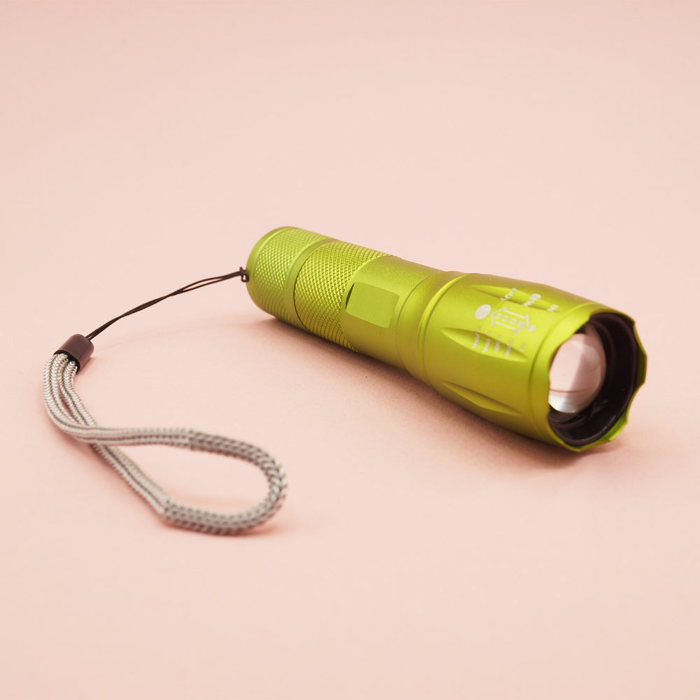 The green flashlight lays on a pink background. The wristlet strap is visible.