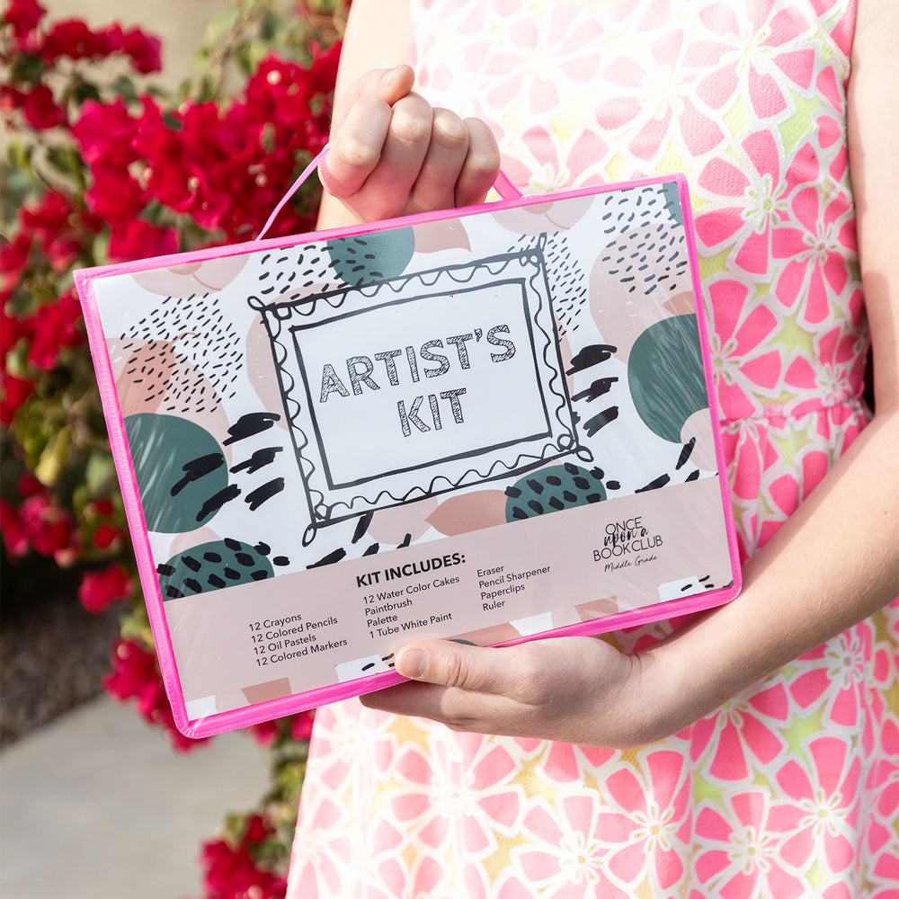 A pair of white hands holds the sealed art kit against their floral dress to showcase the outside design stating "Artist's Kit" and a full breakdown of the contents.