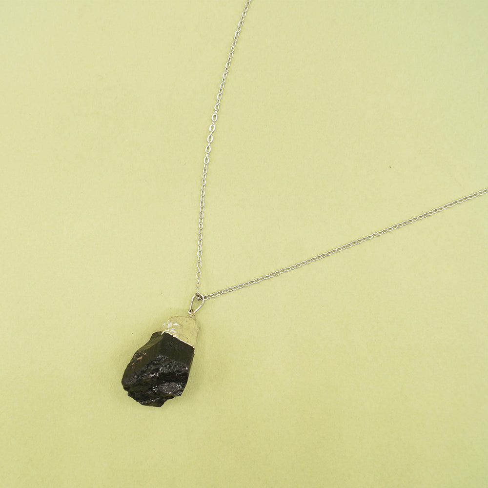 The black tourmaline pendant on the silver chain sits on a green background.