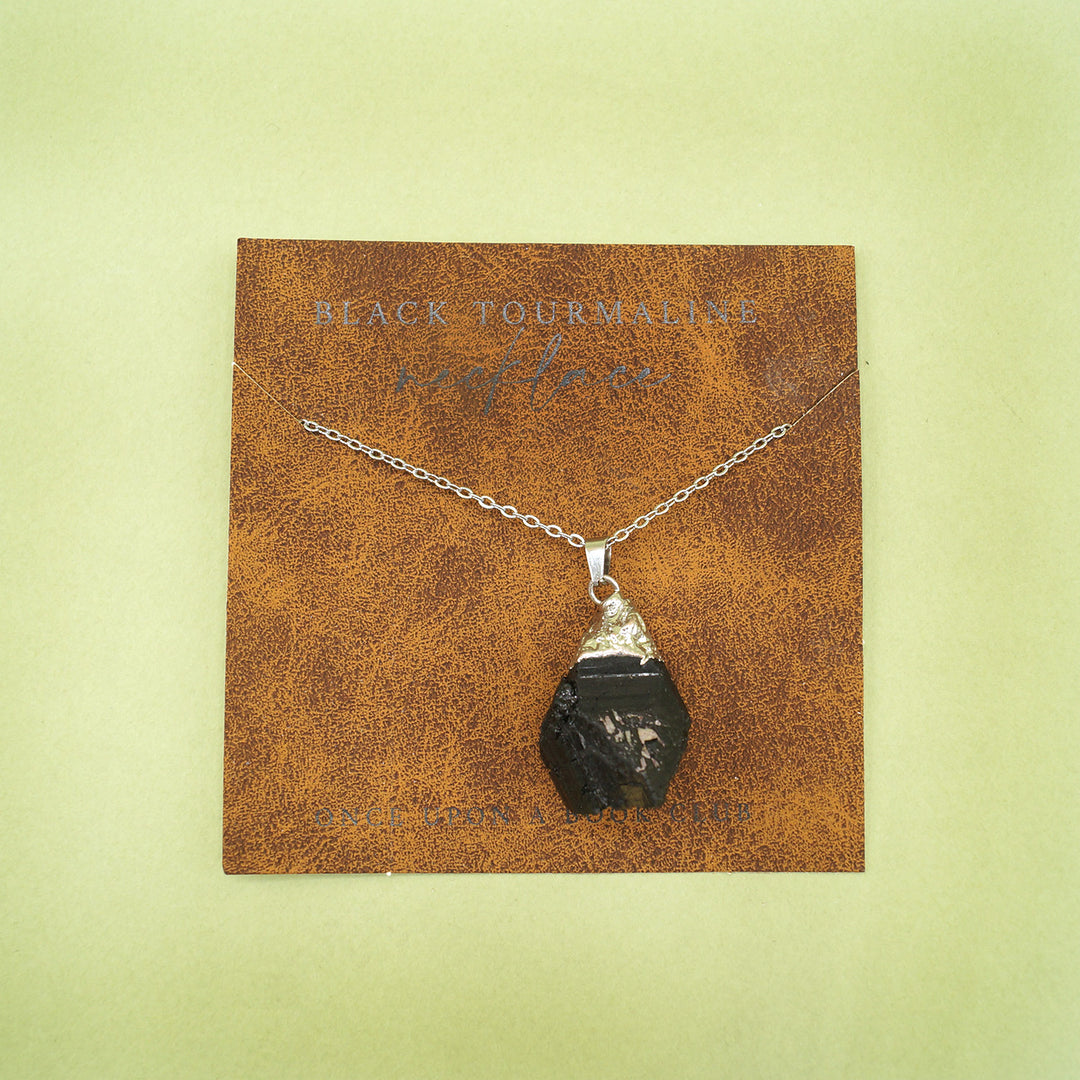 the black tourmaline pendant sits on a card printed to look like leather. The black tourmaline is strung on a silver chain.