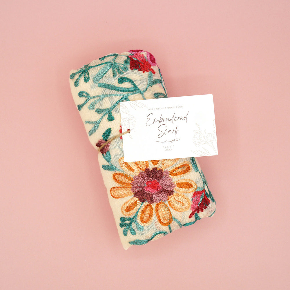The embroidered scarf sits folded on a pink background. The tag is prominently displayed.