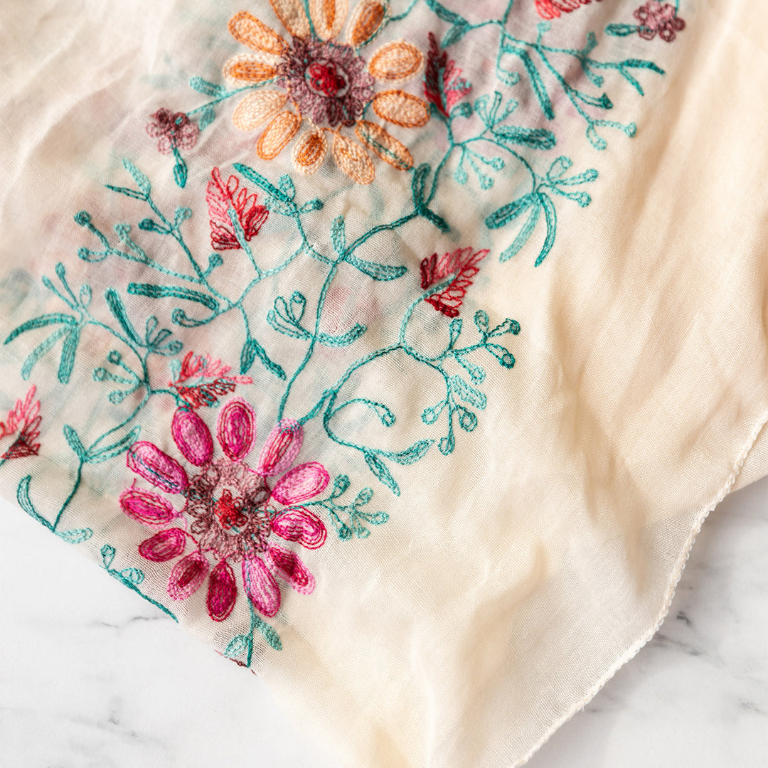 A close up of the intricate floral embroidery pattern on the cream toned scarf.