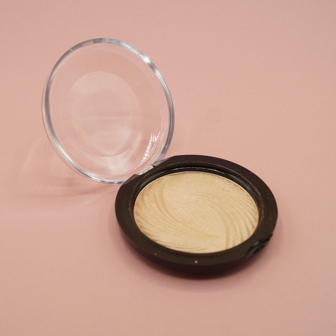 An open makeup compact containing pressed, shimmery highlighter powder. On a pink background.