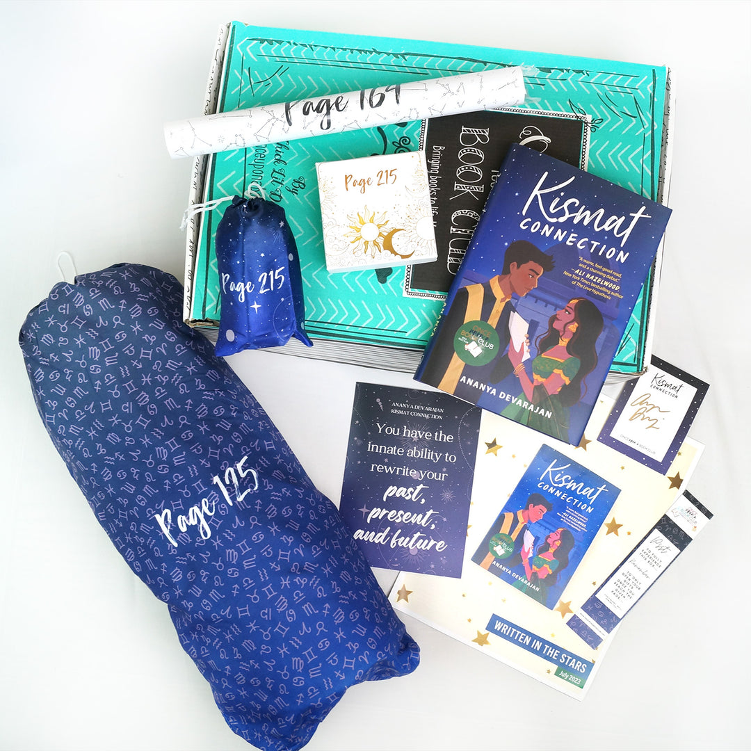 A hardcover edition of Kismat Connection lays on top of a green box next to a small drawstring bag, white box, and white tube. In front of the green box are a large zodiac-patterned drawstring bag, quote card, bookclub kit, bookmark, and signature card. The boxes and bags all have page numbers.