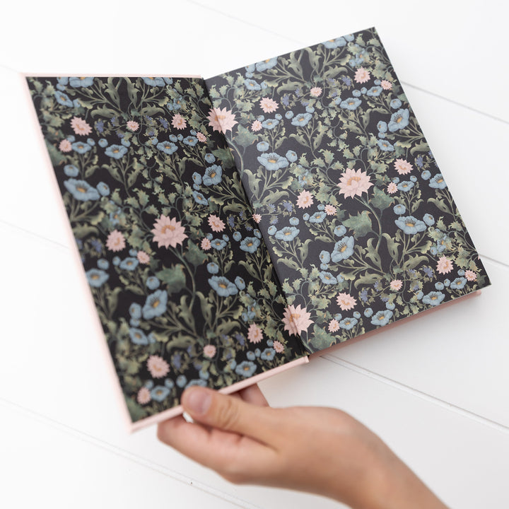 Floral-patterned endpapers of Little Women held by a hand on a white surface