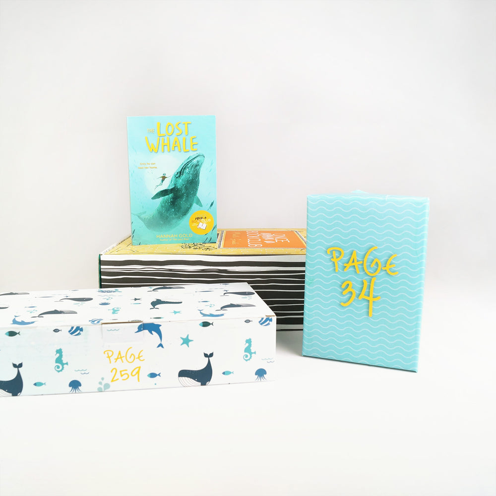 A paperback copy of The Lost Whale by Hannah Gold sits on a yellow Once Upon a Book Club middle grade box. Surrounding this are two wrapped gifts labeled with page numbers