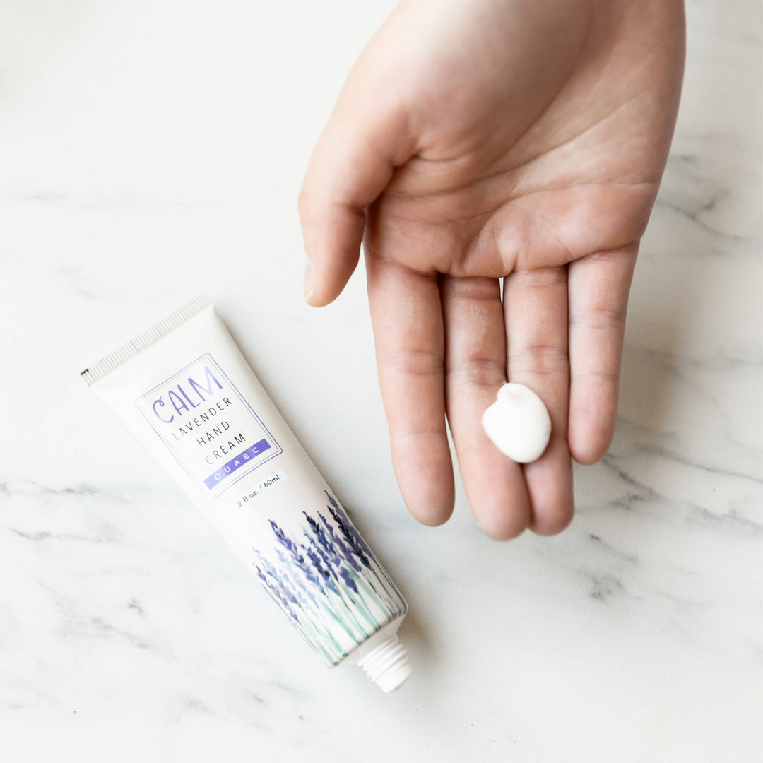 A tube of Calm Lavender Hand Cream sits next to a white hand, holding a dollop of hand cream.
