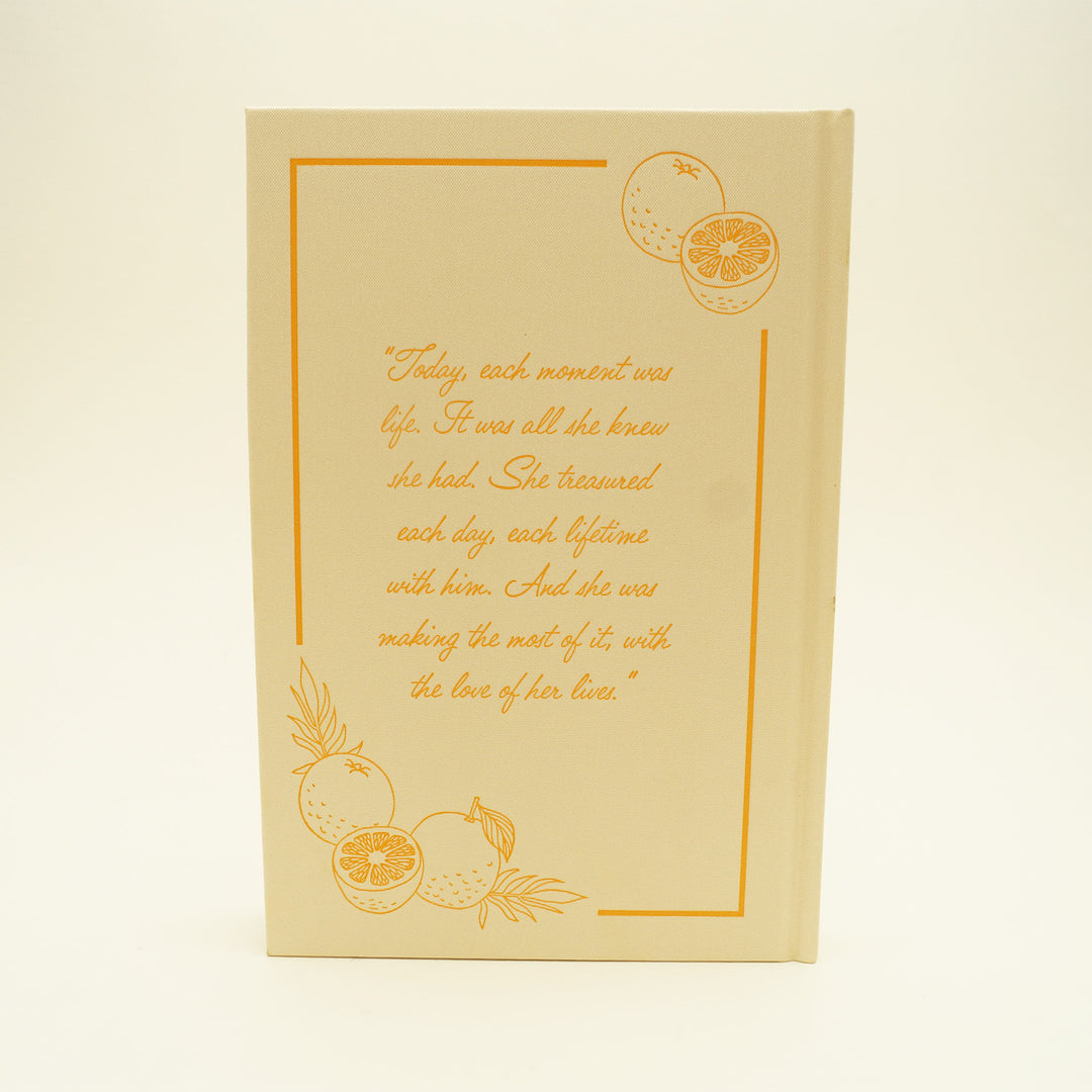 the back of a hardcover pale yellow book with images of oranges on the top right and bottom left. a quote in orange is centered: "Today, each moment was life. It was all she knew she had. She treasured each day, each lifetime with him. And she was making the most of it, with the love of her lives."