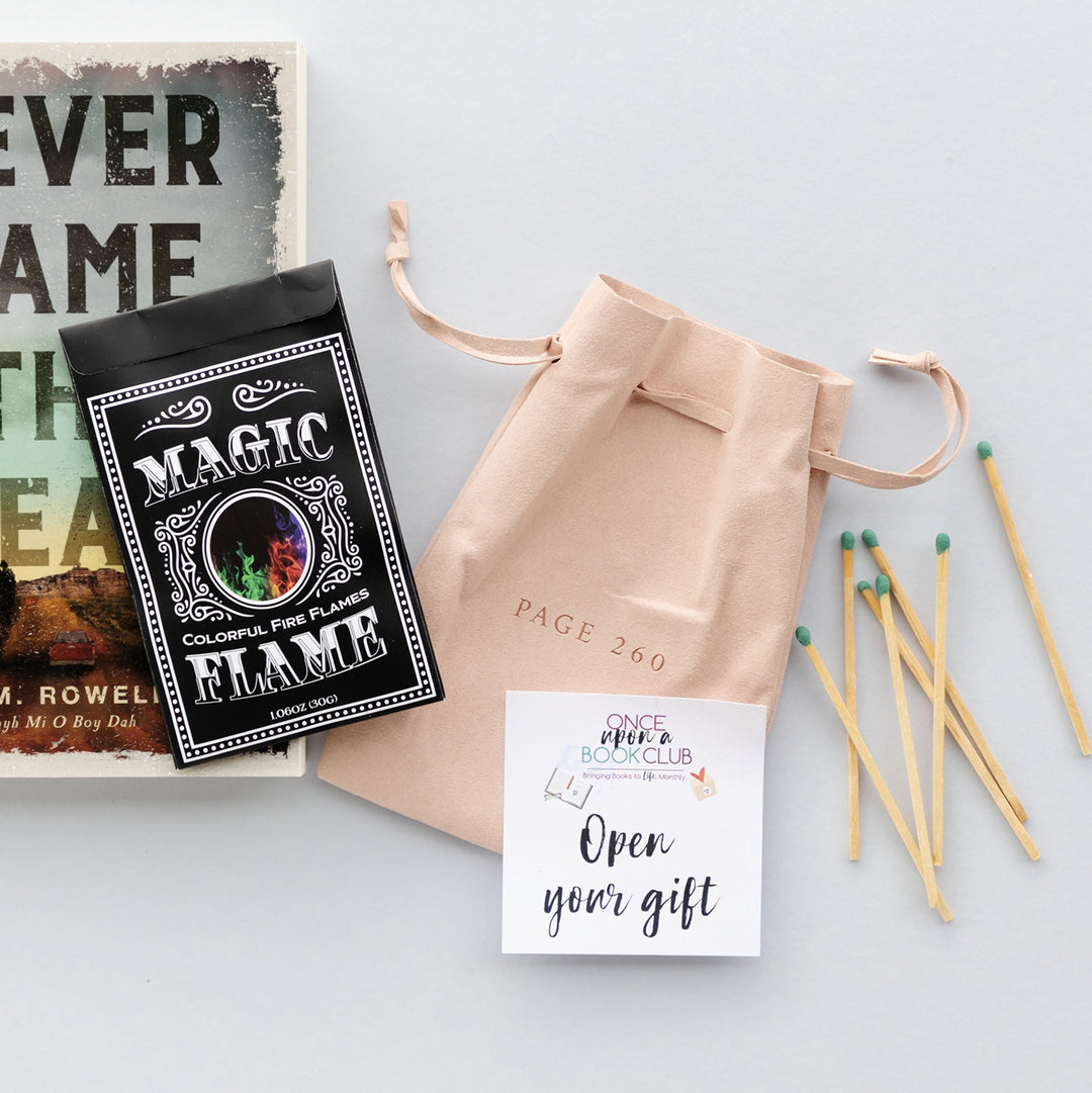 A black packet labeled Magic Flame - colorful fire flames - is on top of a paperback edition of Never Name the Dead, next to a pink drawstring bag, open your gift sticker, and pile of matches