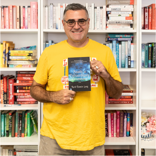 A man wearing a yellow t-shirt smiles while holding a book titled