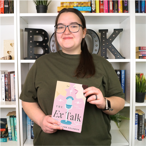A woman wearing an olive green shirt smiles while holding the book