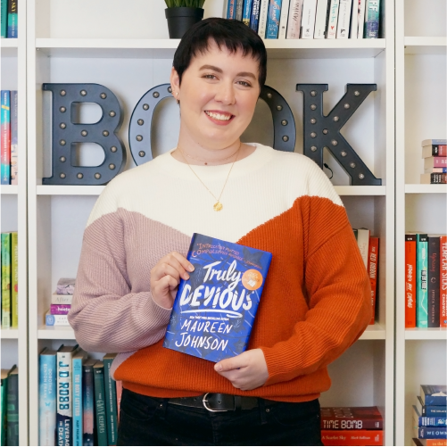 A woman wearing a color-block sweater smiles while holding the book