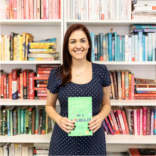 A woman wearing a navy blue polka-dot dress smiles while holding the book