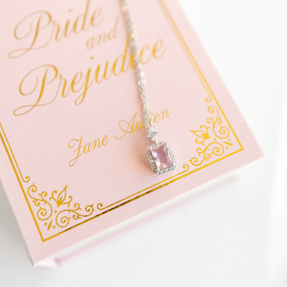 A pink stone on a silver chain lays on a Pride and Prejudice mini jewelry box.