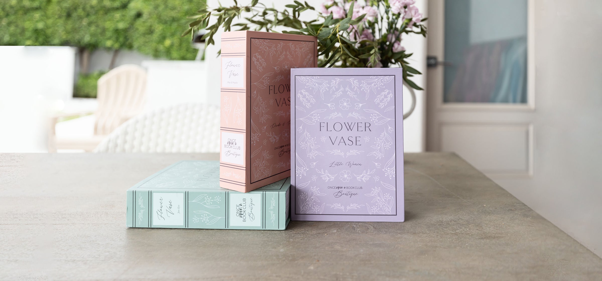 Flower vase packaging from Once Upon a Book Club Boutique displayed on a table with flowers.