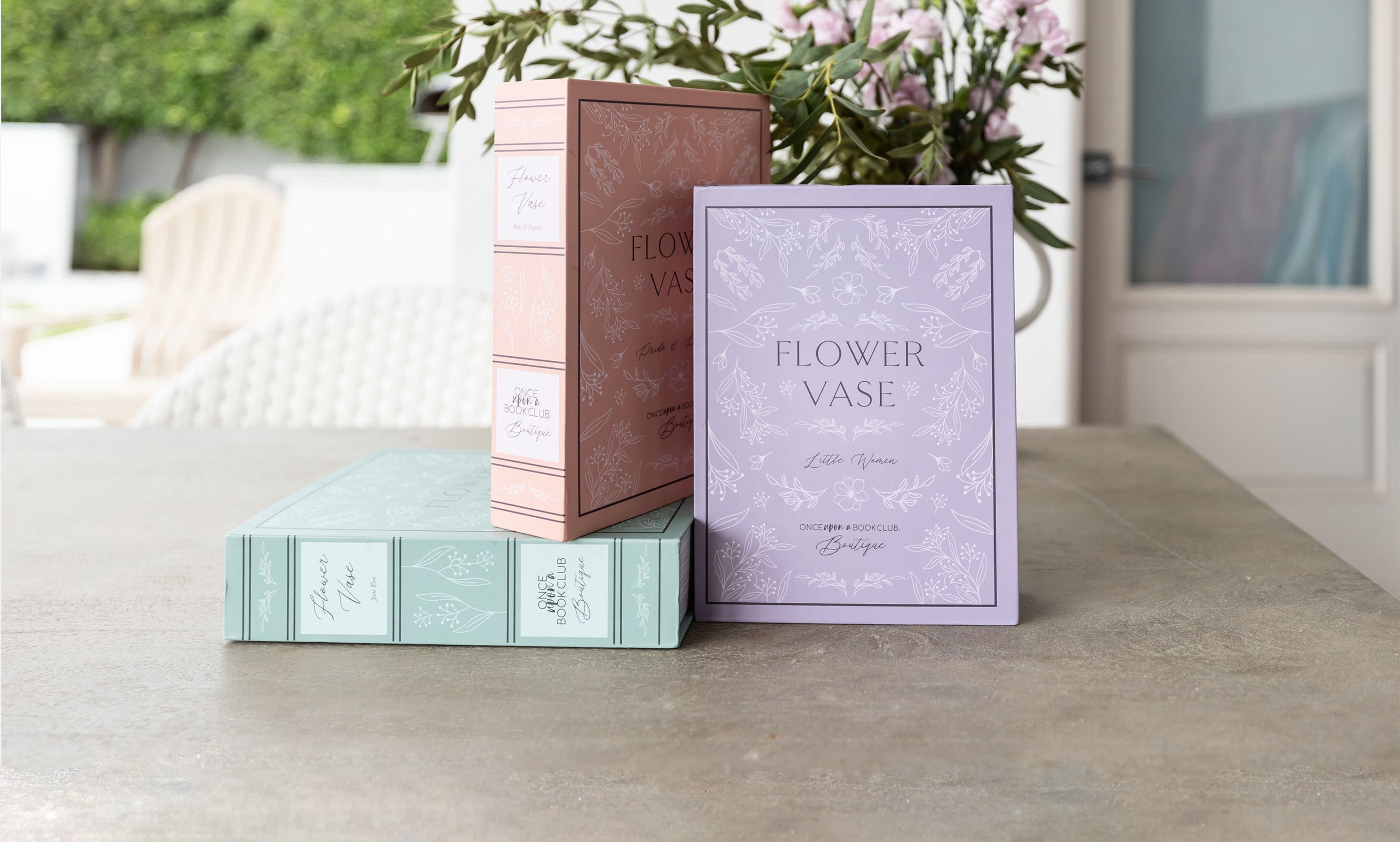 Flower vase packaging from Once Upon a Book Club Boutique displayed on a table with flowers.