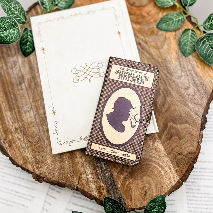 Sherlock Holmes-themed clutch with silhouette design on a wooden surface surrounded by green leaves.