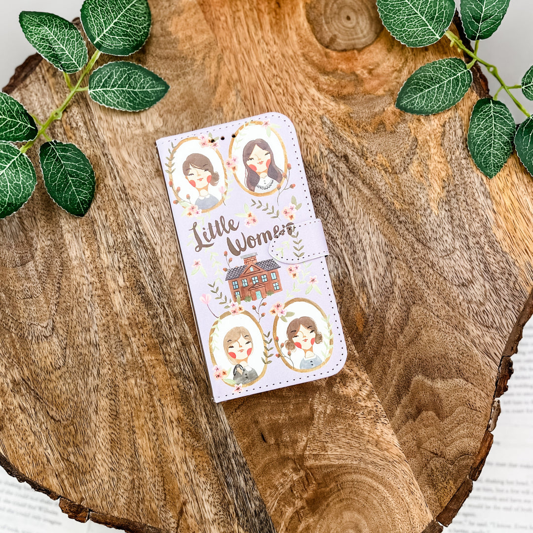 Little Women clutch with character illustrations on a wooden surface with green leaves.