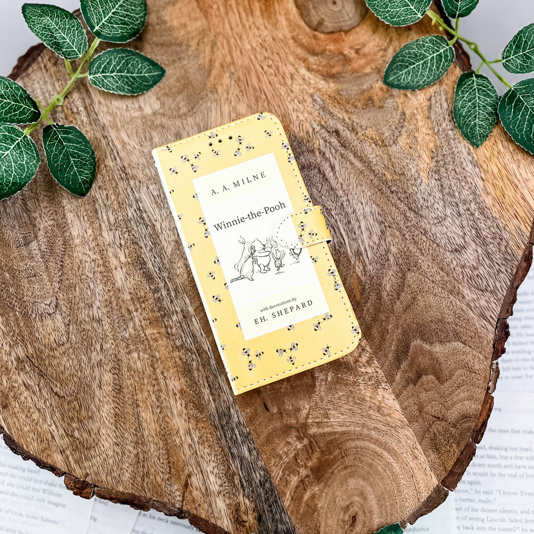 Winnie-the-Pooh book-themed clutch with yellow bee design on a wooden surface with green leaves.