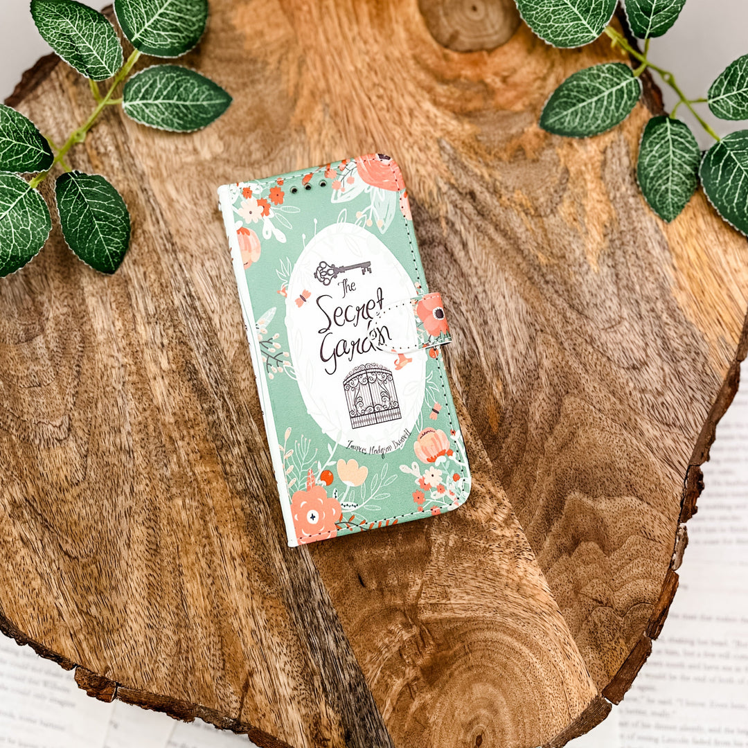 "The Secret Garden" floral-themed book clutch on a rustic wooden surface, accented by green leaves.
