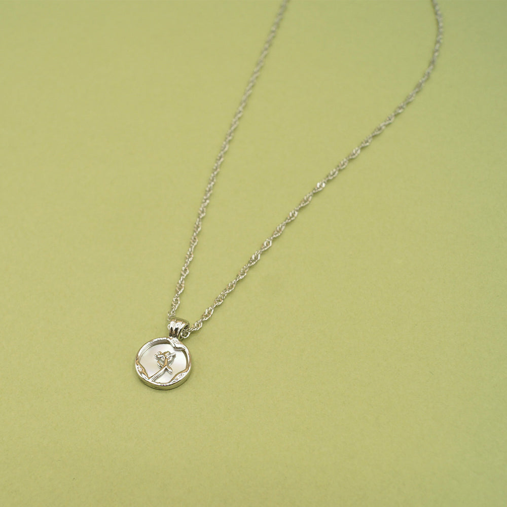 The silver pendant featuring a small disc with a rose shape in the middle of it sits on green background.