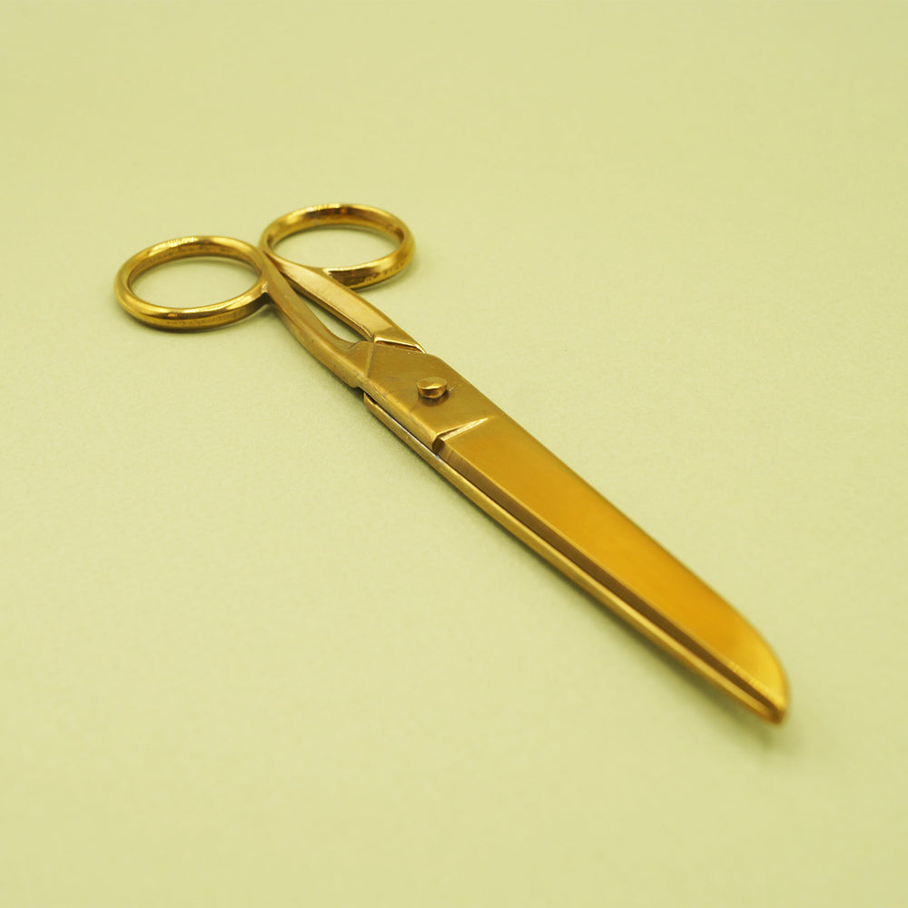 A pair of oversized, gold-toned scissors sits closed on a green background.