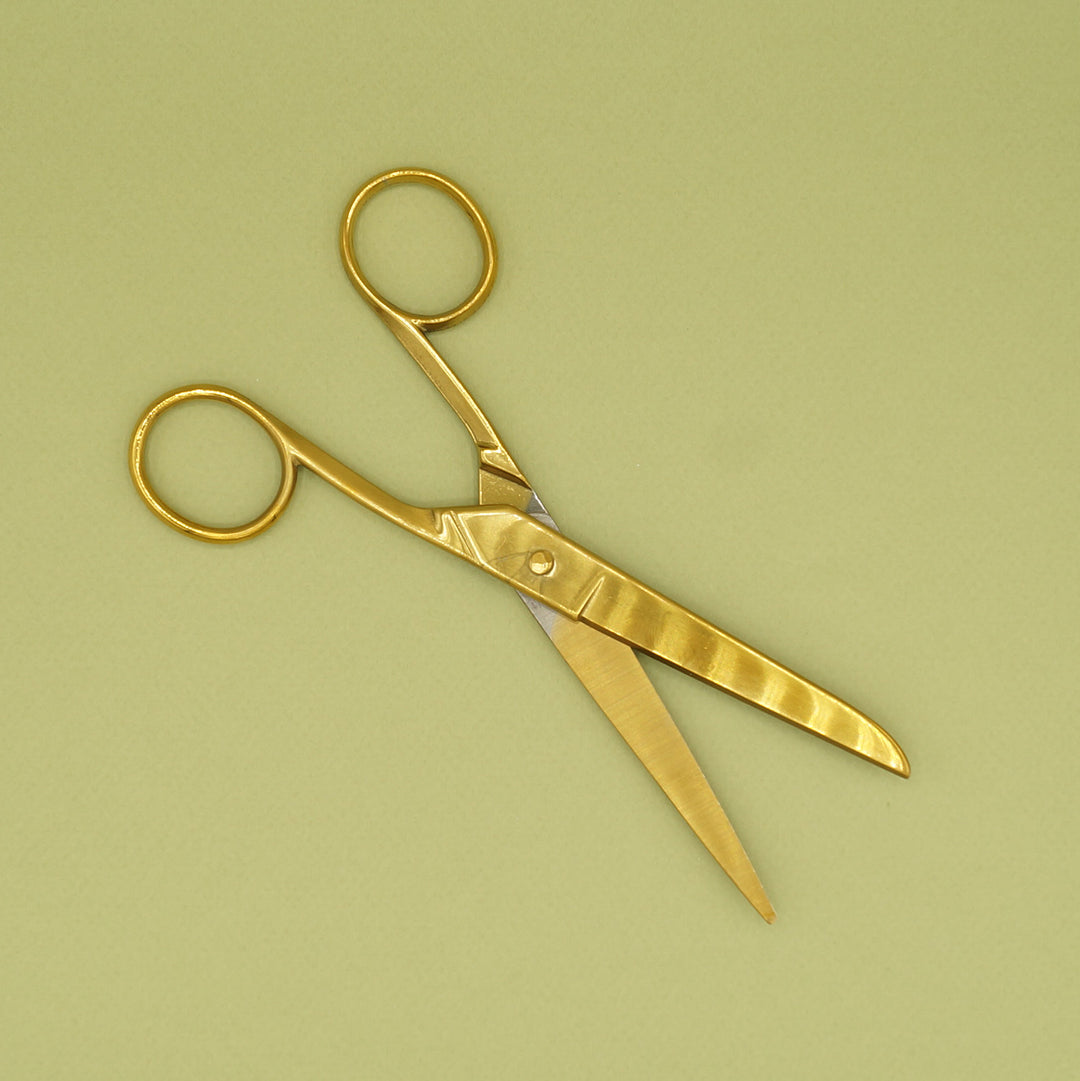 A pair of oversized, gold-toned scissors sits open on a green background.