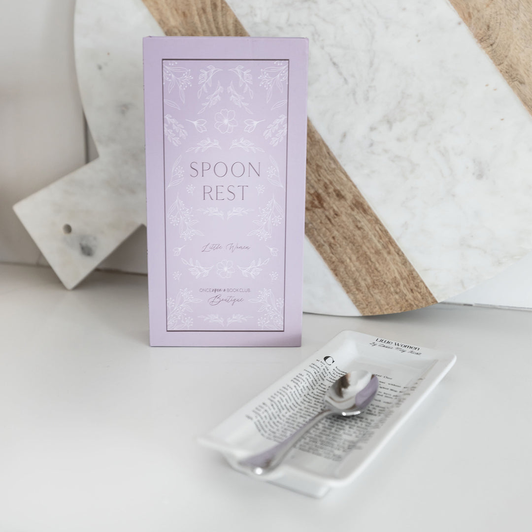 Literary-themed spoon rest with packaging, featuring floral design and text on a marble surface.