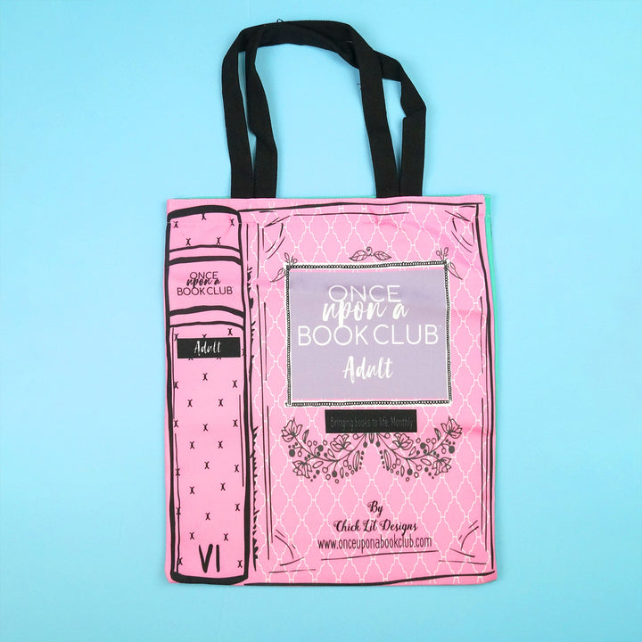 A pink tote bag with a design resembling a book spine featuring the Once Upon a Book Club logo and the word "Adult" on the cover.