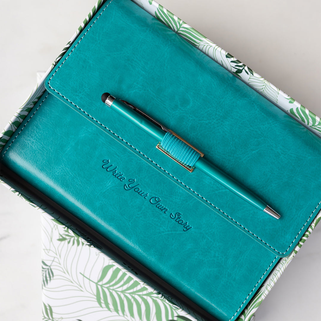 A bright teal, faux leather portfolio journal with matching pen sits closed inside an open box. The portfolio is embossed with the words Write Your Own Story.