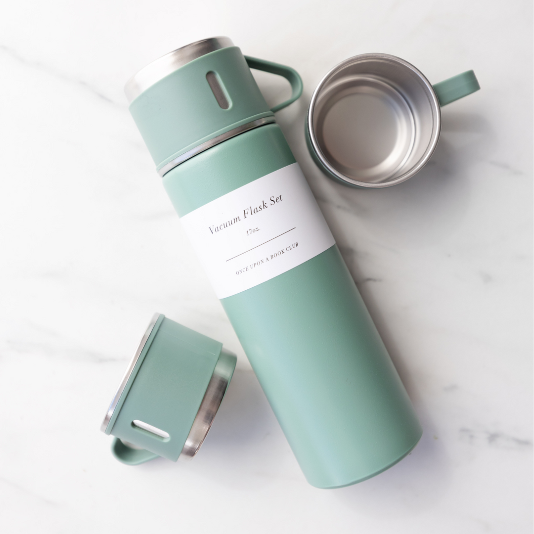 A mint green vacuum coffee flask and two cups lays on a marble countertop.