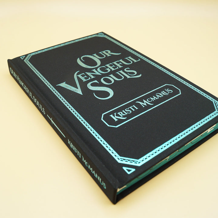 the front hardcase of a hardcover special edition of Our Vengeful Souls. Cover and spine are black with teal writing