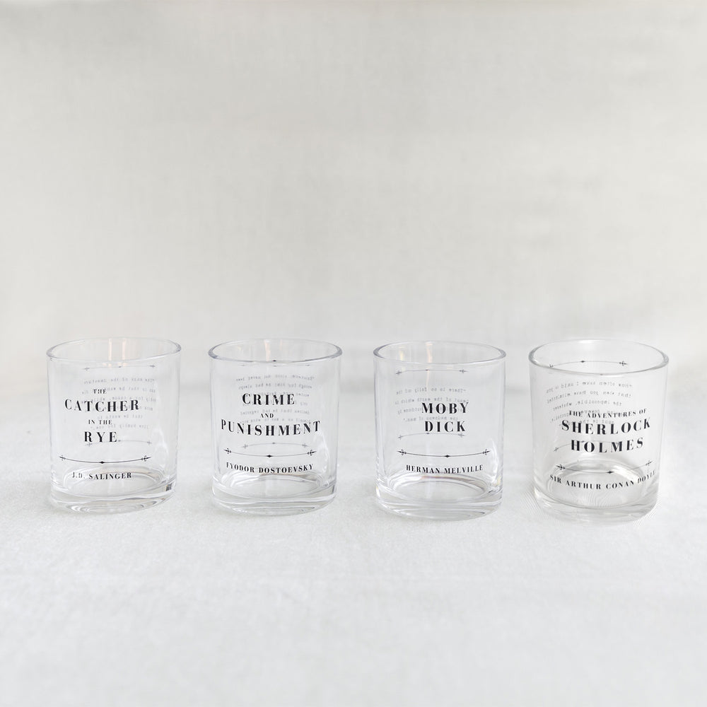 Four clear whiskey glasses with classic book titles printed in black text on a white background.