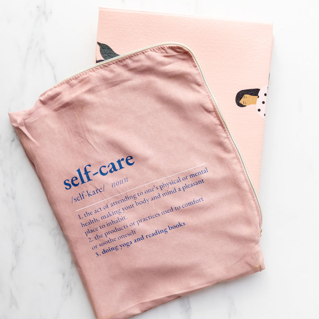 a pink bag labeled self-care along with the definition is on top of a folded up pale pink yoga mat